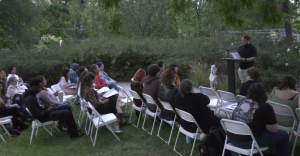 Jacobi Brown reads his poem toast A group of students, staff, and faculty sit on white folding chairs in a garden at College of the Canyons.
